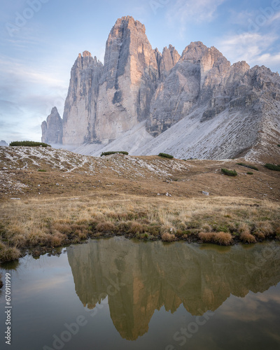 Sun setting over massive rock formation of Tre Cime reflecting in small pond,Dolomites,vertical shot
