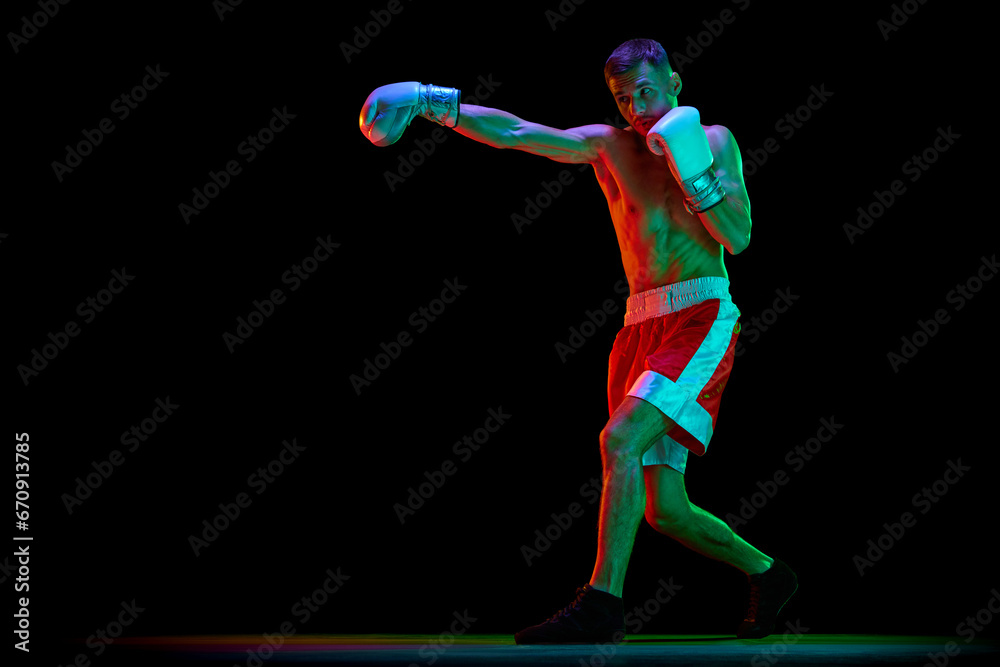 Professional male boxer, mixed martial art fighter training against black mode background in mixed neon filter, light.