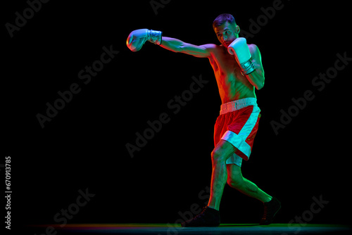 Professional male boxer, mixed martial art fighter training against black mode background in mixed neon filter, light. © Lustre