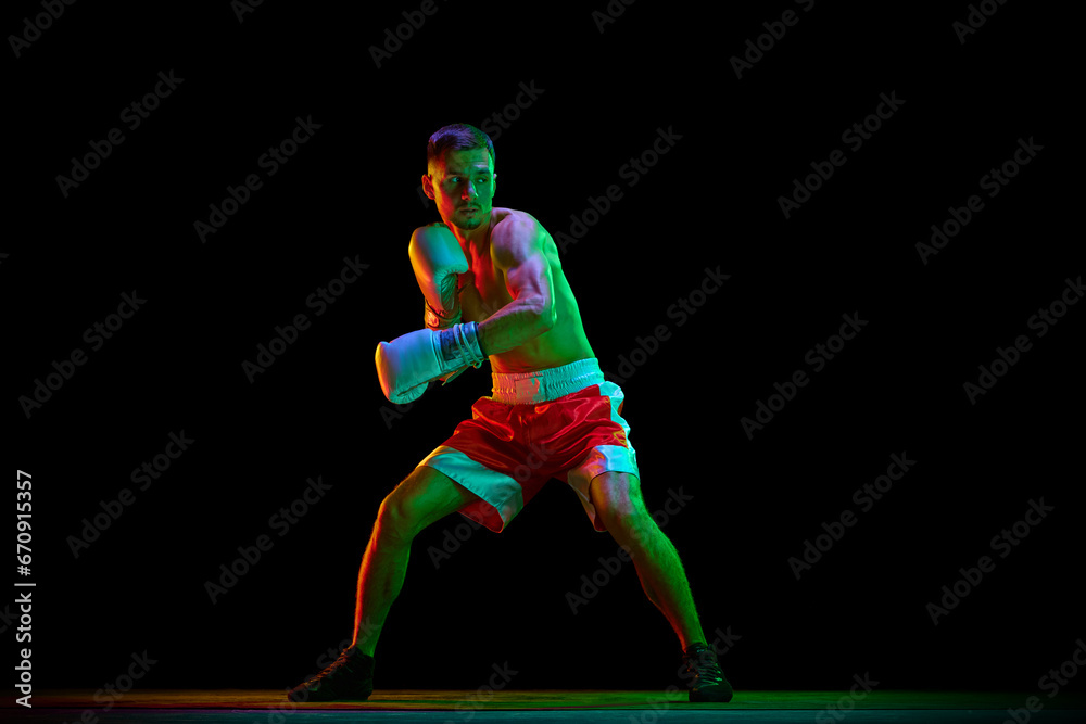 Shirtless boxer, mixed martial art fighter in gloves who preparing to fight against black mode background in mixed neon filter, light.