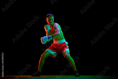 Shirtless boxer, mixed martial art fighter in gloves who preparing to fight against black mode background in mixed neon filter, light. © Lustre