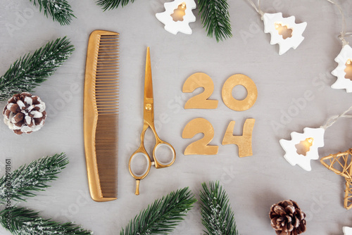 Numbers 2024 golden colored scissors and comb with fir twigs on gray background. Template greeting card of hairdresser or hair salon. photo