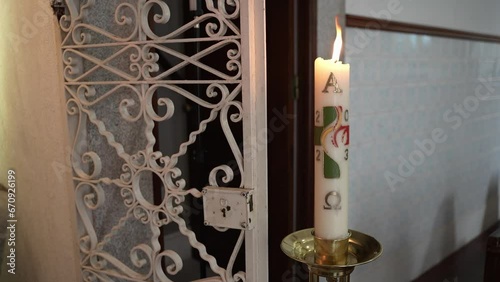 Decorated Paschal candle burning beside ornate metal grille inside church photo