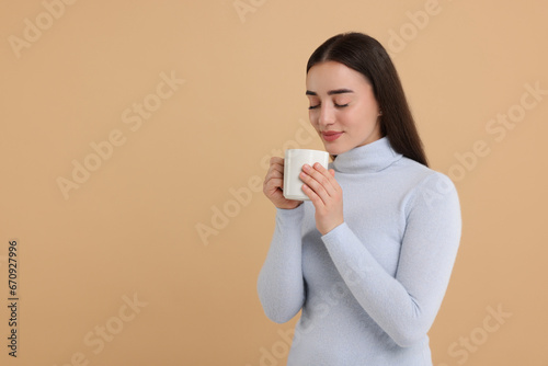 Beautiful young woman holding white ceramic mug on beige background, space for text