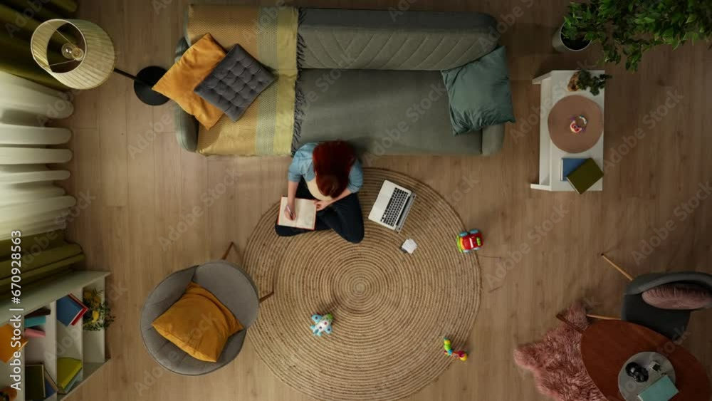 In the shot above, a pregnant woman sits on the floor leaning against a sofa. Nearby is a laptop, she is looking at something in it and writing in a notebook, looking for information. In the shot above, a pregnant woman sits on the floor leaning against a sofa. Nearby is a laptop, she is looking at something in it and writing in a notebook, looking for information.