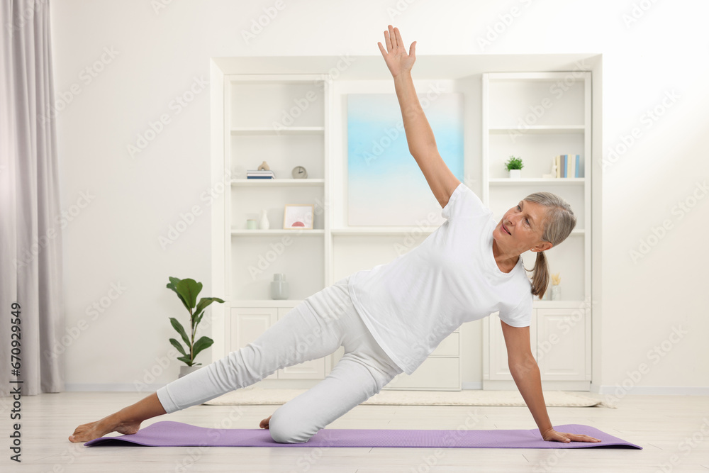 Happy senior woman practicing yoga on mat at home