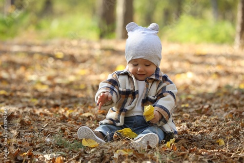 Cute little child on ground with dry leaves in autumn park