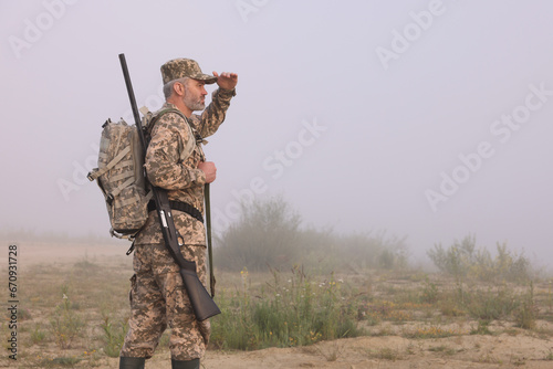 Man wearing camouflage with hunting rifle and backpack outdoors. Space for text