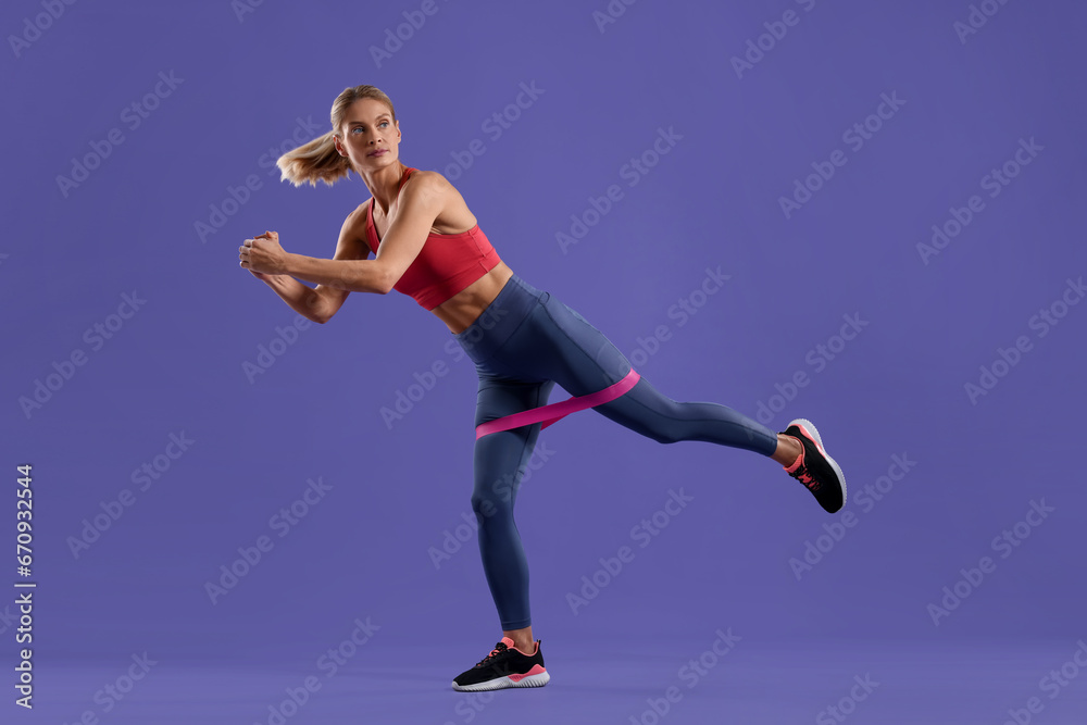 Athletic woman exercising with elastic resistance band on purple background