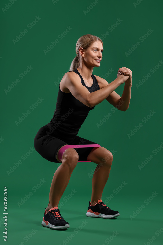 Athletic woman exercising with elastic resistance band on green background Athletic woman exercising with elastic resistance band on green background