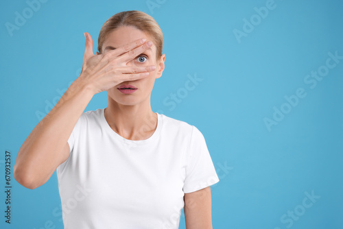 Embarrassed woman covering face on light blue background. Space for text