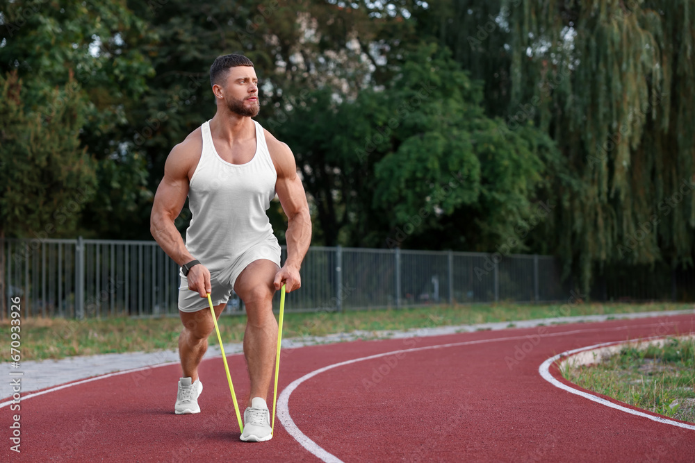 Muscular man doing exercise with elastic resistance band at stadium