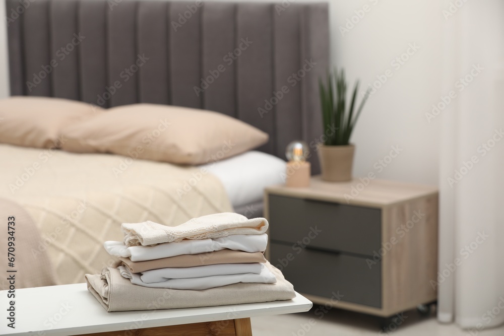 Stack of different folded clothes on bedside bench indoors, closeup. Space for text Stack of different folded clothes on bedside bench indoors, closeup. Space for text