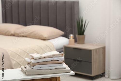 Stack of different folded clothes on bedside bench indoors, closeup. Space for text