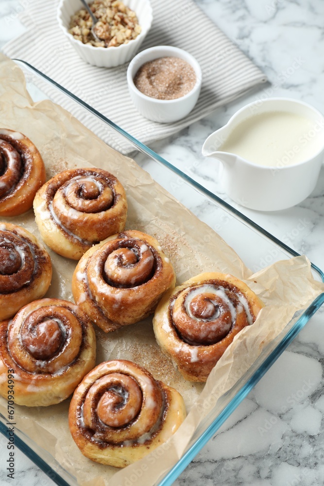 Fototapeta premium Tasty cinnamon rolls in baking dish served on white marble table, above view