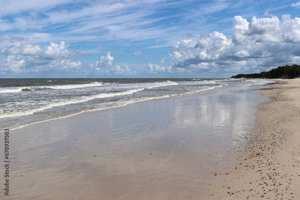 Blue sky and white clouds reflected in the wet sand of a beach on the Baltic Sea coast