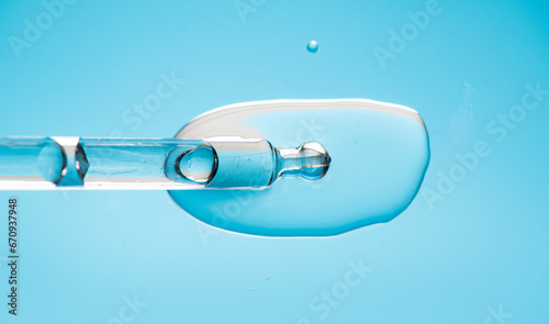Cosmetic dropper with serum, beauty cosmetics dripping, on blue background. Macro shot. Serum, peptides, beauty and health care products. Glass pipette with liquid close up. Top view. Skin care 