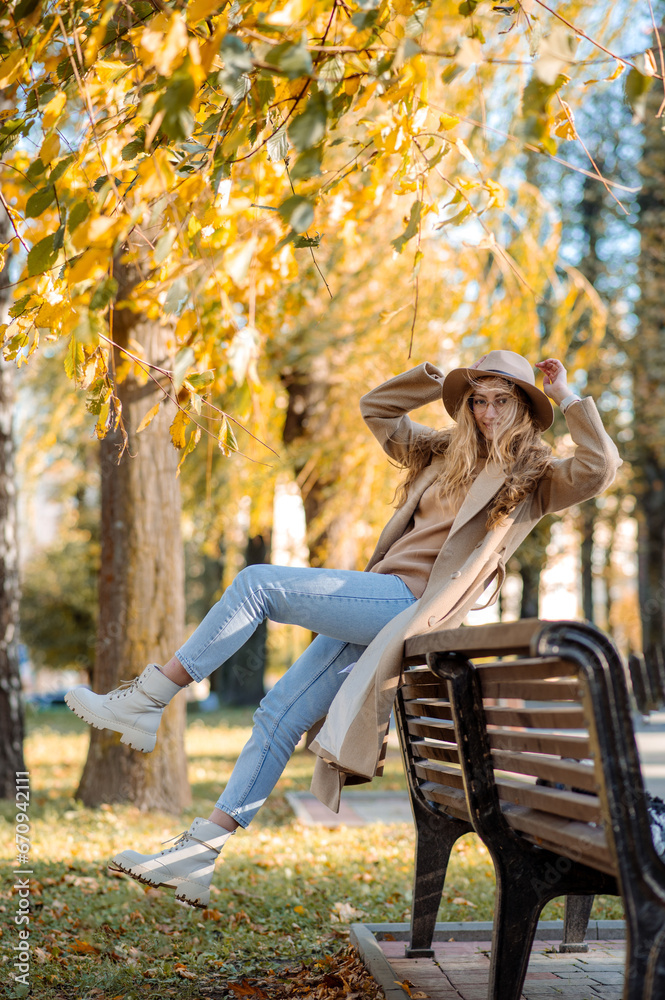 Beautiful adult blonde woman in a hat and coat sits on a bench in an autumn park and has fun Beautiful adult blonde woman in a hat and coat sits on a bench in an autumn park and has fun