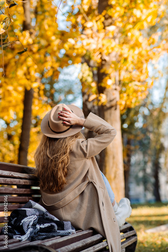 Beautiful adult blonde woman in a hat and coat sits on a bench in an autumn park and has fun