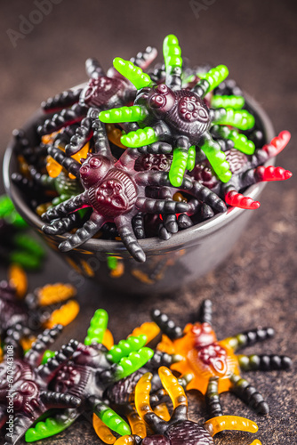 Scary sweet jelly spiders. Halloween candies in bowl on black table.