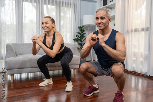 Athletic and sporty senior couple engaging in leg day training session with squat together at home exercise as concept of healthy fit body lifestyle after retirement. Clout