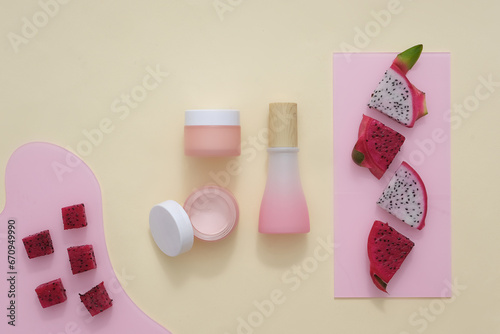 Fresh dragon fruits with different shapes are placed on a pink acrylic sheet. Unlabeled cosmetic bottles displayed on a beige background. Develop cosmetics with fresh fruit.