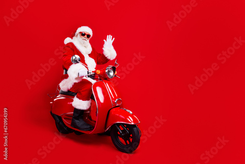 Full size photo of funky grandfather wear stylish santa costume glasses riding on red scooter say hello isolated on red color background