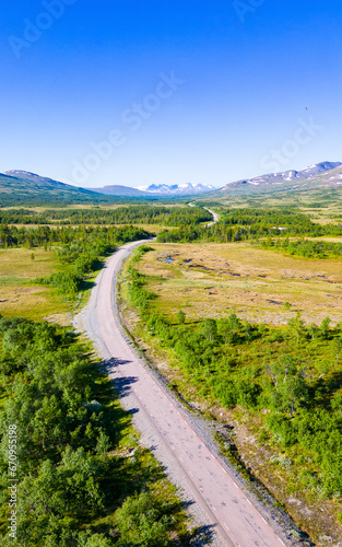 Typical scandinavian landscape with a road leading through forests and wetland with mountains in the background