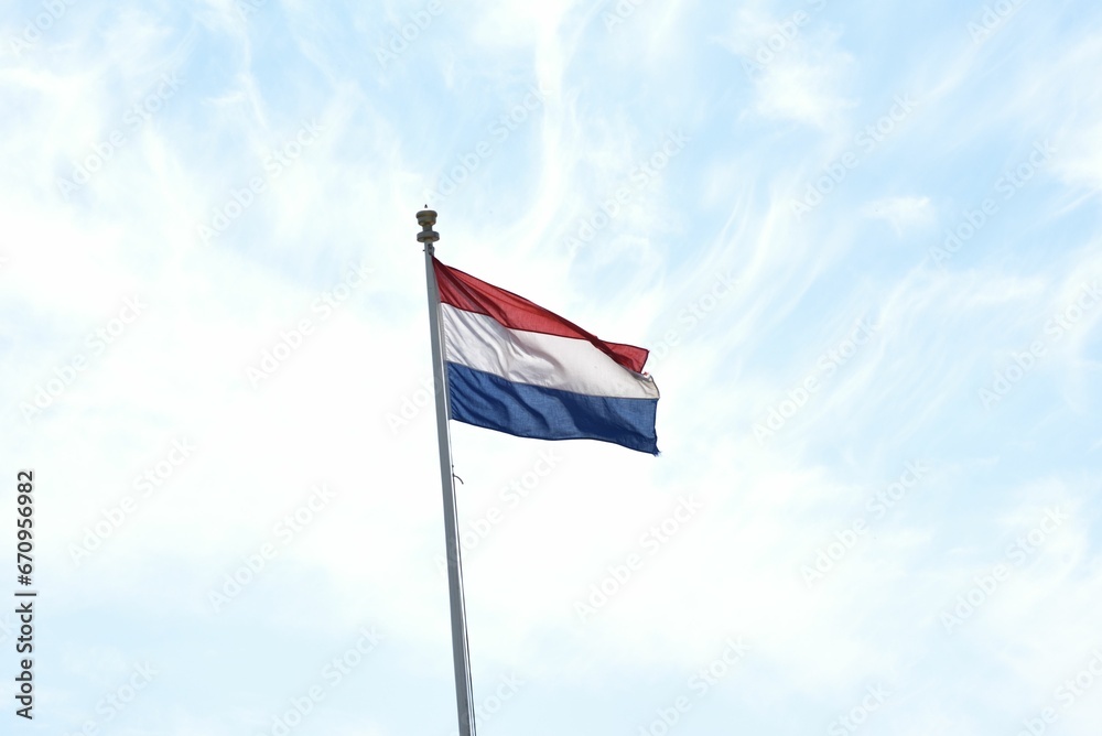 Vibrant flag of Netherlands waving against a clear blue sky depicting an iconic and patriotic scene