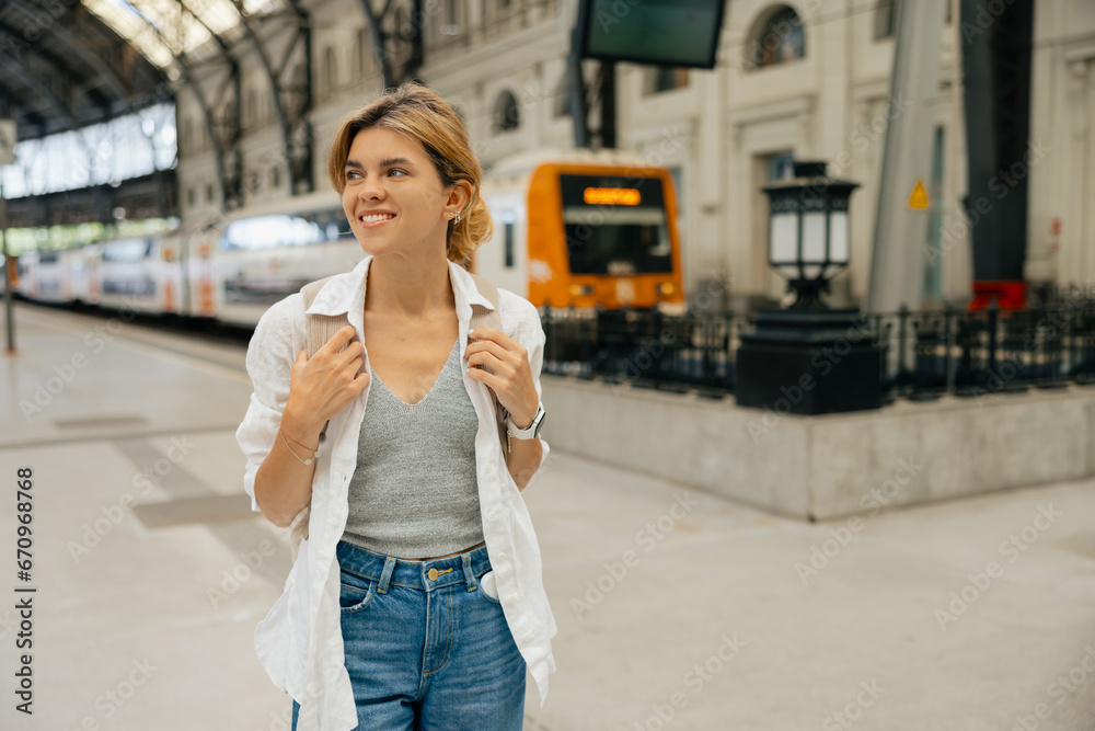 Cute  woman standing at train station. Blonde with wavy hair, wears denim jacket. Concept of modern technologies