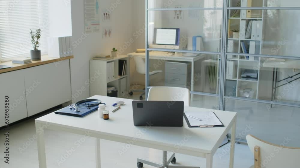 No people shot of contemporary physician office interior with laptop and medical documents on white table and medical couch behind glass partition wall