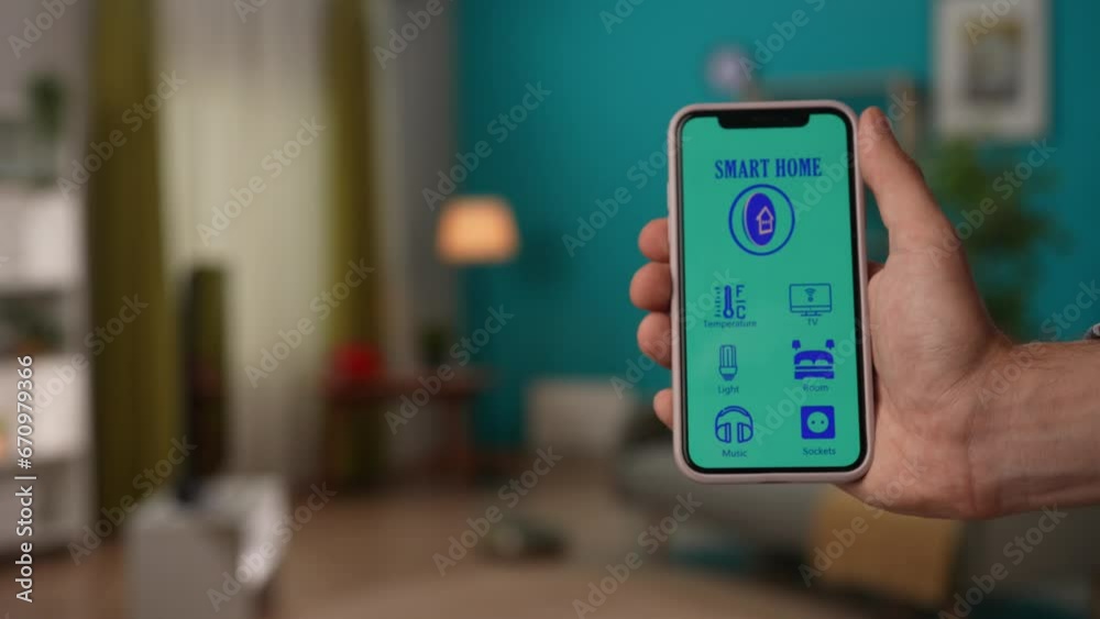 Focus on man hand holding smartphone, smart home app loading on the screen showing user interface with different icons. Smart house concept. Focus on man hand holding smartphone, smart home app loading on the screen showing user interface with different icons. Smart house concept.