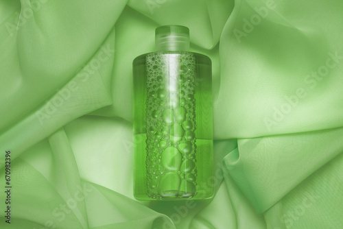 Plastic cosmetic bottle with skin tonic, antibacterial gel on a background of green silk fabric with folds with an empty space for text, copy space, flat lay, the concept of skin care, prevention 