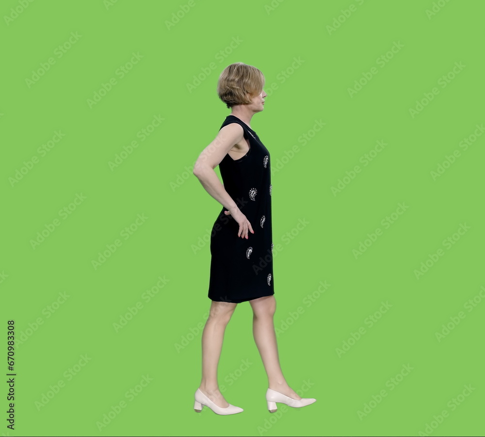 Side view of elegant adult woman in dress walking with hand on hip on green background, Chroma key Side view of elegant adult woman in dress walking with hand on hip on green background, Chroma key