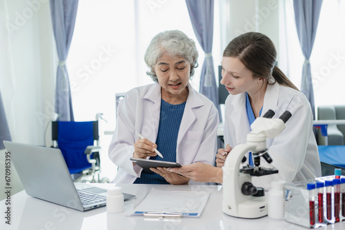 Laboratory, old female doctor and woman doing medical research with blood in tube, beautiful young woman in white coat sitting in office and working with blood sample in laboratory medical laboratory