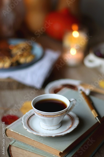 Cup of tea or coffee, plate with desserts, dried oranges, bowl of grapes, scented candles, vintage books, pumpkins and autumn leaves on the table. Autumnal hygge. Selective focus.