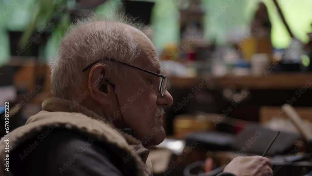 An old craftsman in a wheelchair at work in his workshop An old craftsman in a wheelchair at work in his workshop