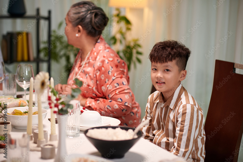 Little boy sitting at dinner table next to his grandmother