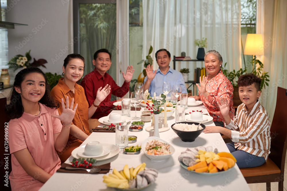 Big Vietnamese family sitting at dinner table and waving at camera