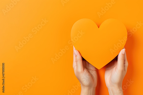 hand holds a heart love shape on an orange background with copy space