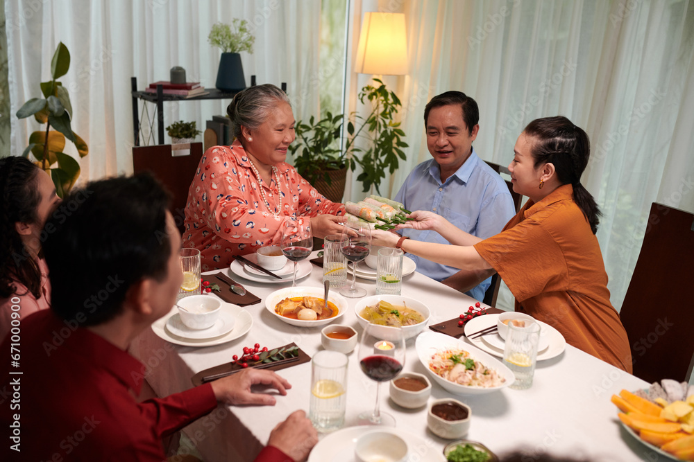 Cheerful Vietnamese family eating traditional spring rolls when dining together Cheerful Vietnamese family eating traditional spring rolls when dining together