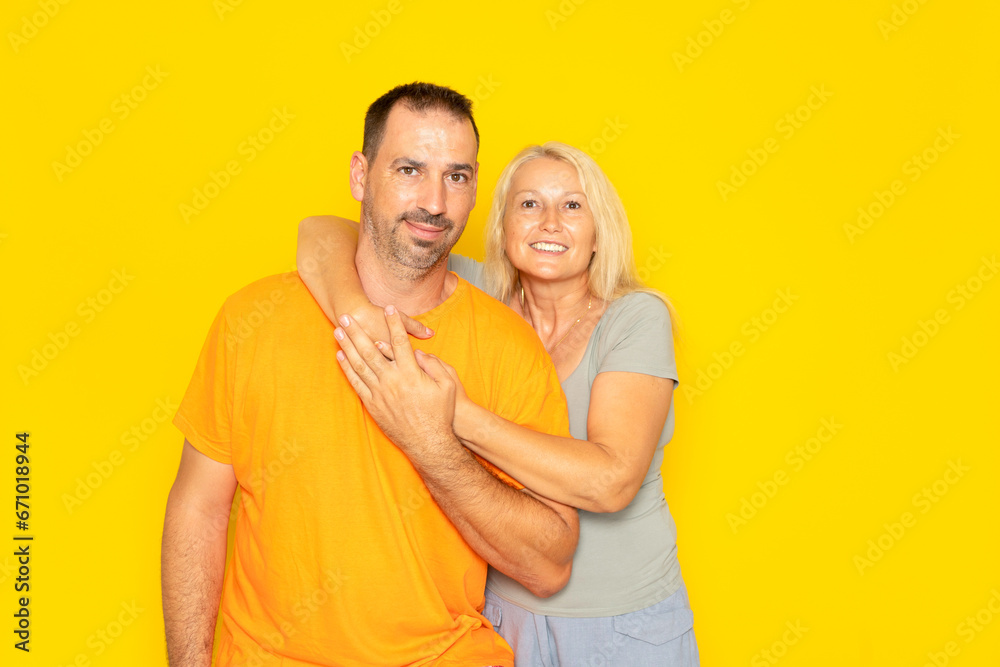 White happy couple hugging and looking at camera isolated over yellow background. White happy couple hugging and looking at camera isolated over yellow background.