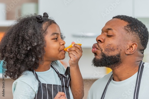 african afro hair black kid Cute taste oranges citrus sour flavour on lips mouth with daddy in kitchen. back african daughter kid afro hair and daddy frowning face for taste is sour of sliced orange photo