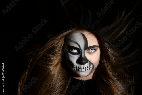 Portrait of a girl with makeup in the form of a skull and developing hair on a black background