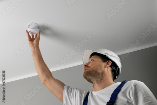 fire safety engineer installing photoelectric smoke detector on house ceiling. home security and fire alarm system