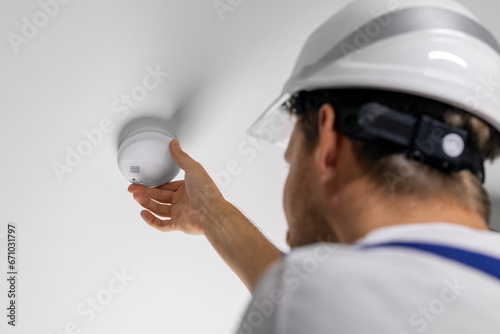 worker installing photoelectric smoke detector on house ceiling. home security and fire alarm system photo