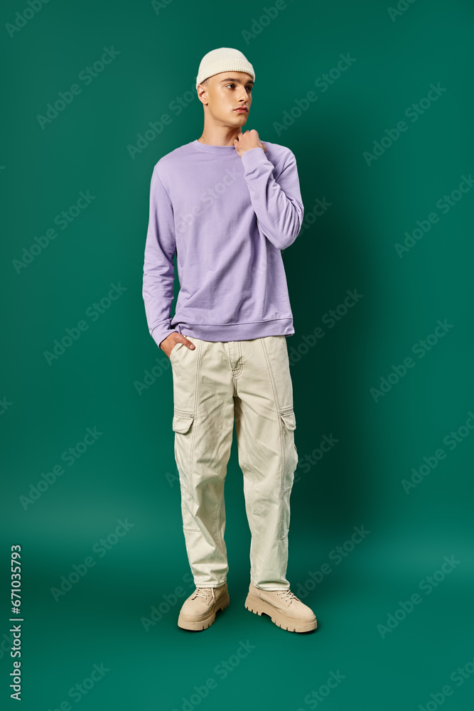 full length of tall man in beanie and purple sweatshirt posing with hand in pocket on turquoise full length of tall man in beanie and purple sweatshirt posing with hand in pocket on turquoise