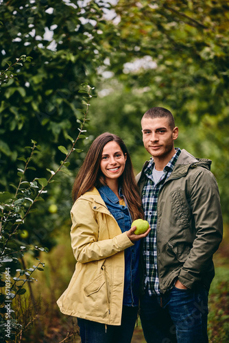 Portrait of two smiling lovers, standing in the orchard together, holding a quince.