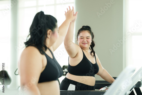 Overweight Asian friends wearing sports gear compete on the treadmill in the village gym. The happiness of women exercising and losing weight in their free time. Lifestyle and exercise concepts