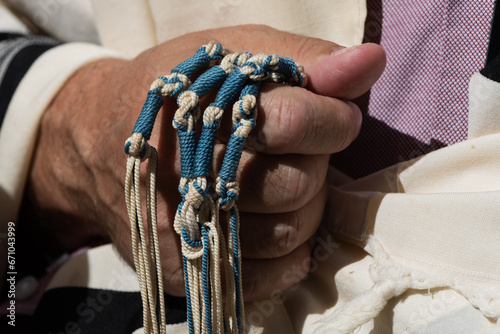 An Orthodox, Jewish man holds blue techelet tzitzit strings while reciting the Shema Yisrael during Jewish morning prayer. photo